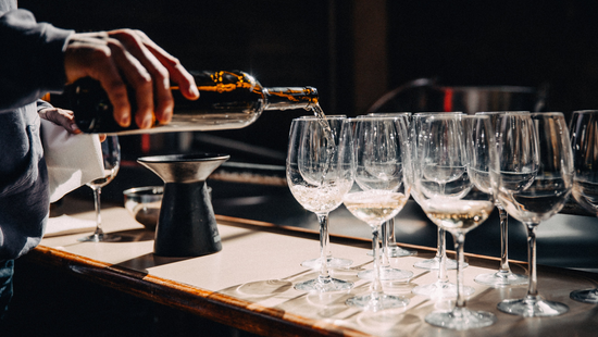 Person pouring wine into a glass with multiple glasses on a bar counter.