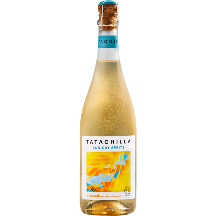 A bottle of Tatachilla Sun Day Spritz non-alcoholic sparkling wine, featuring a light golden-amber liquid, a white label with a vibrant yellow, orange, and blue graphic, and a cork stopper.