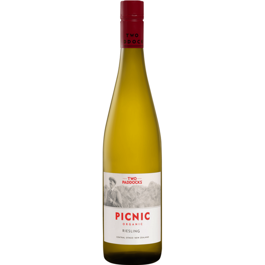 A bottle of Two Paddocks Picnic Organic Riesling white wine, featuring a pale golden-yellow liquid, a white label with red and black text, and a dark red screw cap, set against a solid green background.